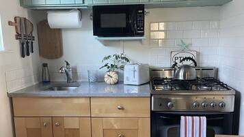 Cocina compacta con gabinetes verde azulado, un microondas, un tostador, un hervidor y una estufa a gas.
