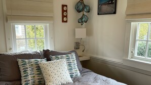 Un dormitorio con una cama grande, dos mesitas de noche, un reloj de pared, una lámpara colgante y una ventana con persianas.
