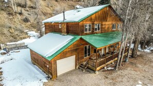 Eine zweistöckige Blockhütte mit einem grünen Dach, einer Veranda und einer Garage.