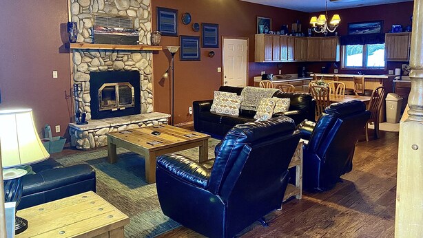 Ein Wohnzimmer mit Kamin aus Stein, Ledermöbeln und einer Küche im Hintergrund.
