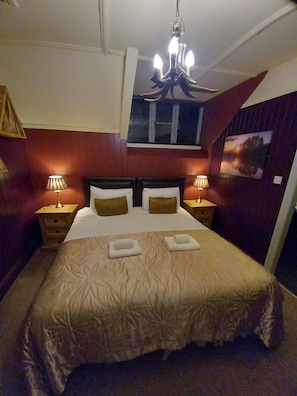 A hotel room with a large bed, two bedside tables, a chandelier, a window with blinds, and a painting on the wall. - No 1 Hotel (Wooler)
