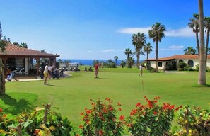 Un campo de golf con vista despejada al océano, palmeras y un edificio de techo rojo.