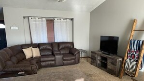 A living room with a brown leather sofa, a flat-screen TV, and a wooden cabinet. - Cozy ranch style house in a quiet neighborhood (Sioux Falls)