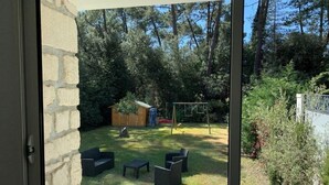A view through a glass door into a backyard with a grassy lawn, a wooden play structure, and outdoor furniture.