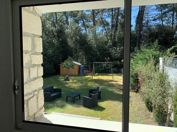 A view through a glass door into a backyard with a grassy lawn, a wooden play structure, and outdoor furniture.