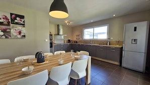 Una cocina moderna con comedor, que incluye una mesa de madera, sillas blancas y un ventanal grande.
