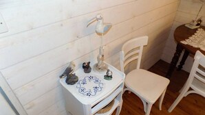A small white table with a decorative lamp, a plate with a blue pattern, and a wicker basket. There are two white chairs and a wooden floor.