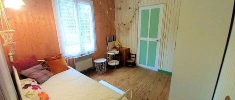 A cozy room with a bed, a small table, a chair, and a window with curtains.
