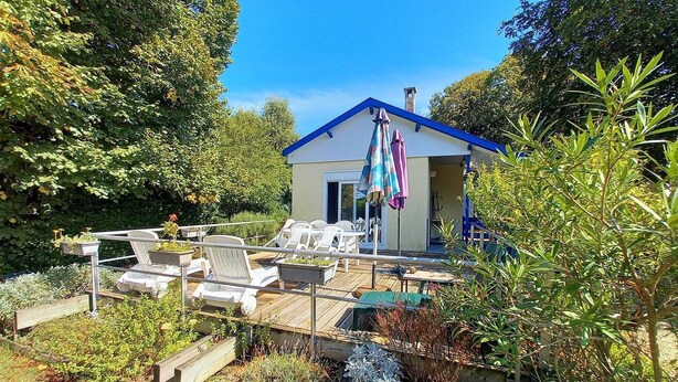 A small house with a blue roof, a deck with white chairs, and a garden with various plants.