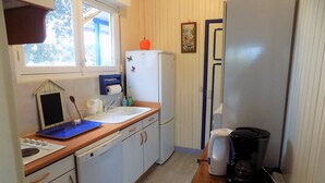 A compact kitchen with a sink, a coffee maker, a refrigerator, and a window with a view of trees.