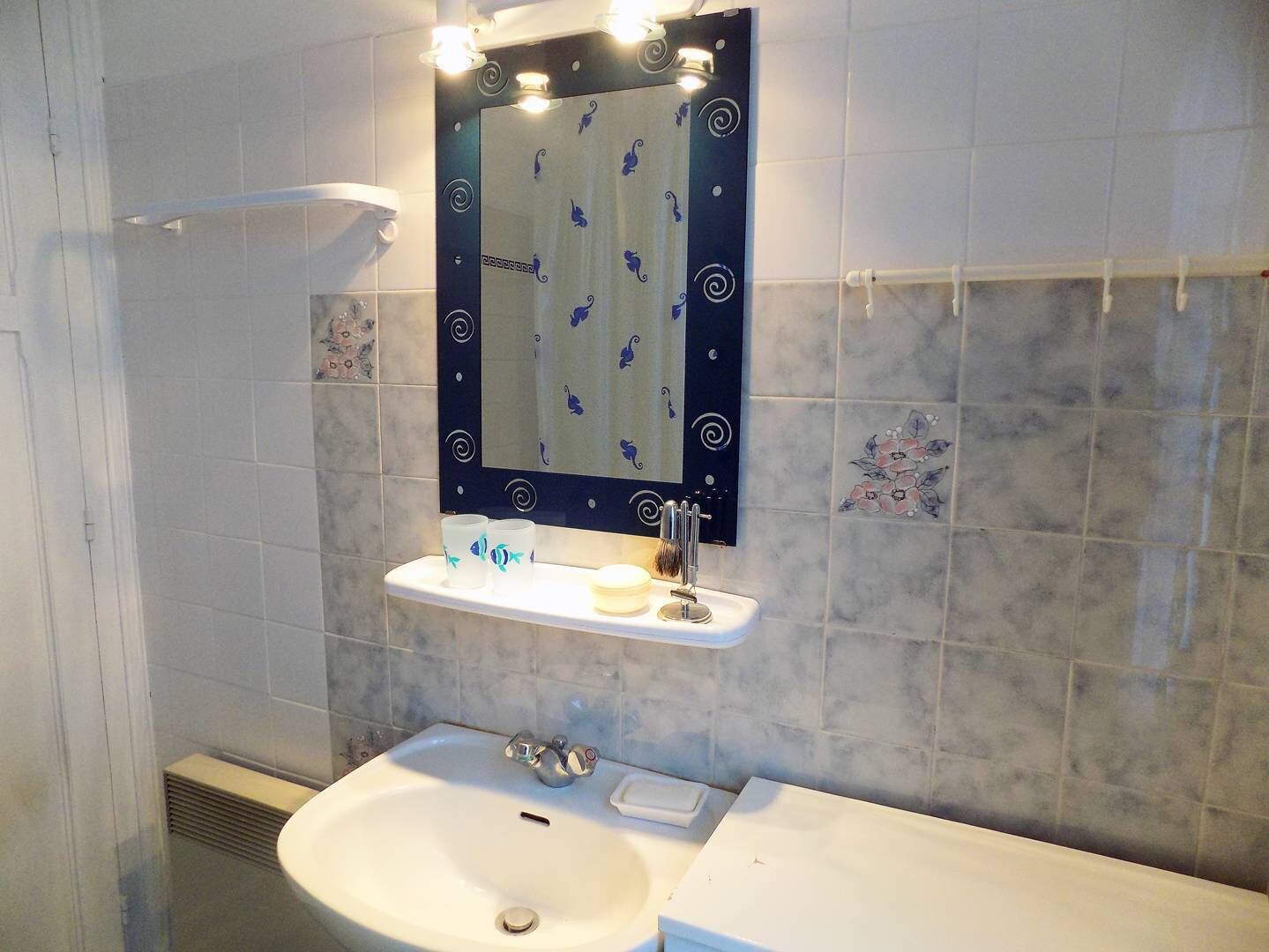 Un baño con un lavamanos blanco, un espejo con marco decorativo y un perchero para toallas.
