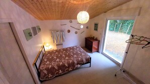 A bedroom with a bed, a dresser, a hanging light fixture, and a window with a view of greenery.