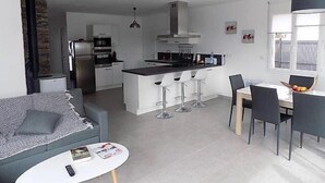 A modern kitchen with a central island, bar stools, and a dining area with a table and chairs. - Saint Palais sur Mer - VERY NICE RECENT HOUSE - near the GOLF (ST PALAIS SUR MER)