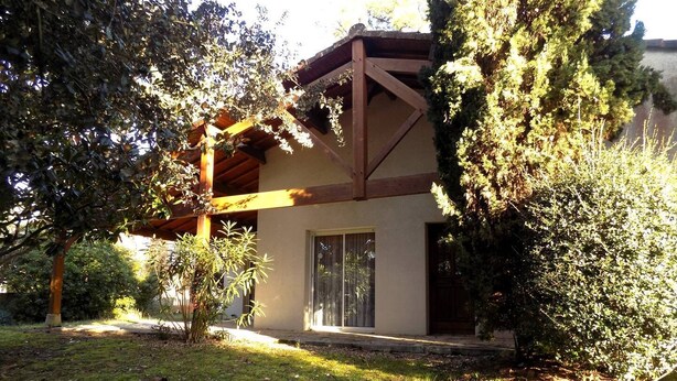 Un bâtiment à ossature en bois, doté d’un patio couvert et d’un jardin agrémenté d’arbres et d’arbustes.