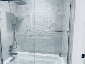 Un espace de douche clos par des parois de verre, avec un mur en marbre, une porte en verre et une pomme de douche visible.