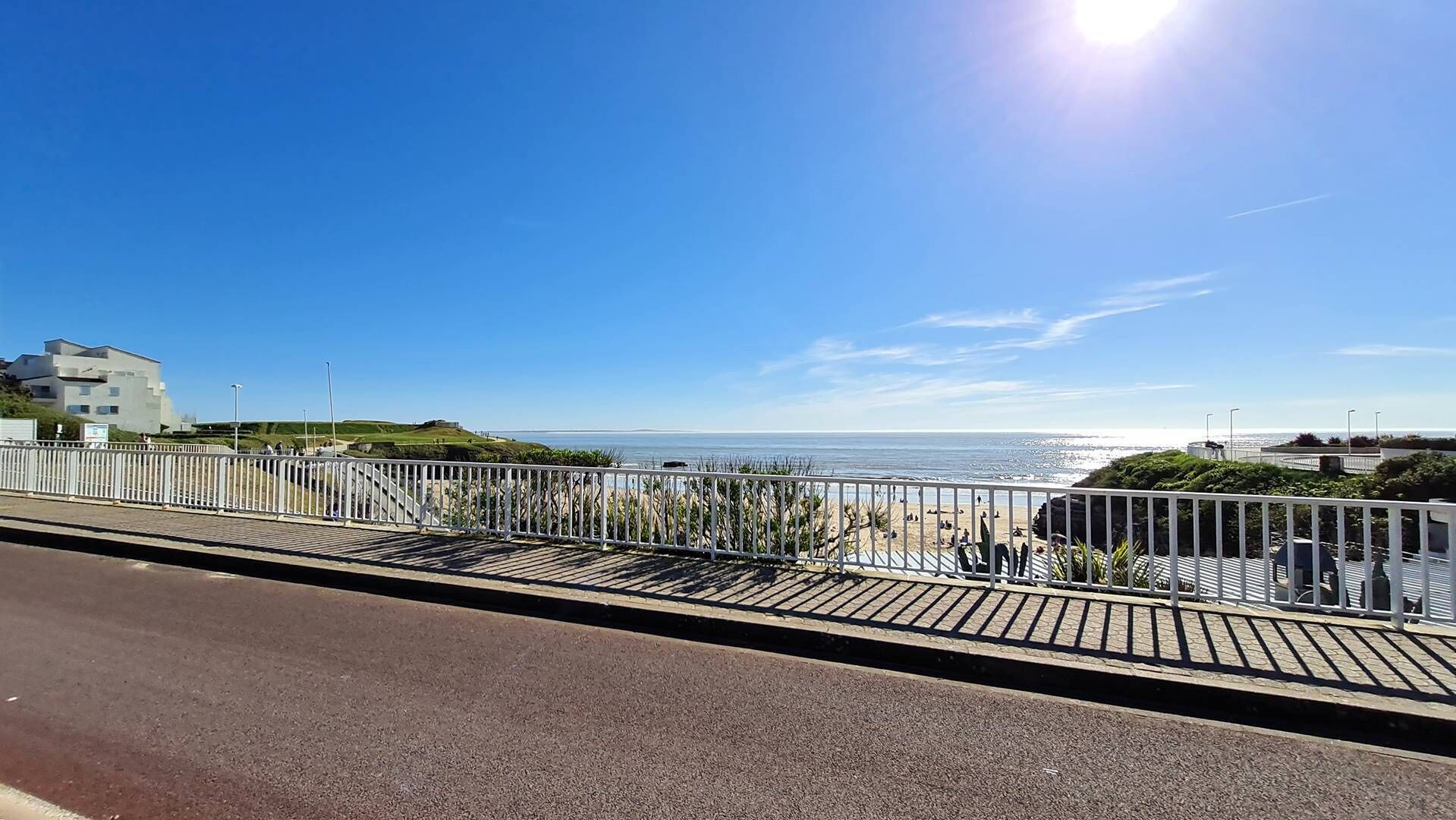 A coastal road with a metal railing, a clear blue sky, and a view of the sea.