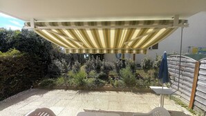 Un patio couvert avec un auvent à rayures, une clôture en métal et diverses plantes.