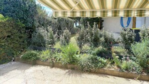 Un espace extérieur abrité, doté d’un auvent à rayures, entouré d’une végétation luxuriante et d’une clôture en métal.