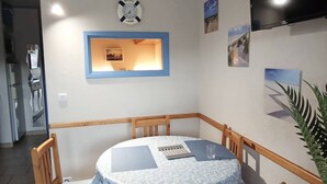 A dining area with a round table, chairs, a clock, and framed pictures on the wall. - AS21387-Studio cabin and private parking 200m sea (LE GRAU DU ROI)