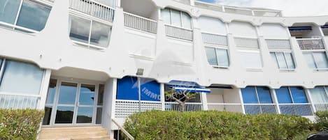 A multi-story building with a modern architectural design, featuring balconies, large windows, and a blue awning.