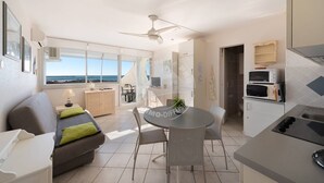 Una cucina moderna con zona pranzo, un divano con cuscini, un tavolino con sedie e vista mare tramite ampie finestre.