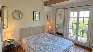 A bedroom with a bed, two bedside lamps, a mirror, and a large window with a view of greenery. - House for 4 people - Sea view - Swimming pool - Air conditioning - WiFi - Near beach - Sainte Maxime (STE MAXIME)