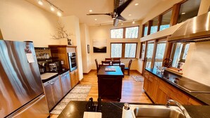A modern kitchen with a central island, stainless steel appliances, and large windows.