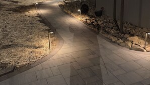 A paved pathway leading to a building with a stone retaining wall and a sign indicating the front door.