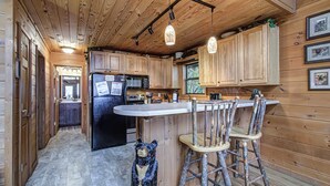 A wooden cabin kitchen with a central island, bar stools, and a bear statue. - Where Mountain views and quiet moments come naturally, it’s s’more than enough (Sevierville)