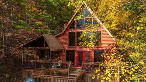 A cabin with a wooden deck, a red door, and a large window. - Where Mountain views and quiet moments come naturally, it’s s’more than enough (Sevierville)
