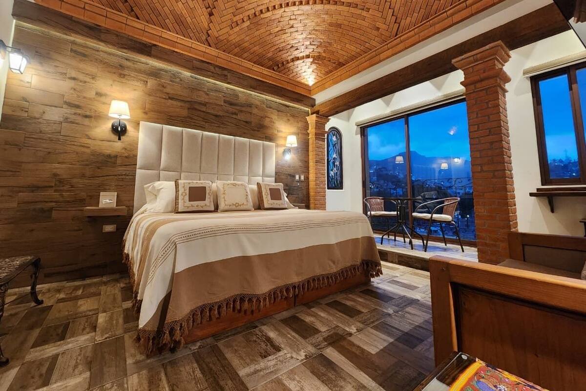 Un dormitorio con una cama grande, techo de madera y vistas a la ciudad a través de amplios ventanales.