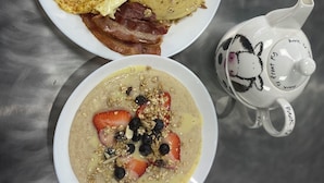 Un plato de desayuno con tortitas, fresas, arándanos y bacon, junto a un tazón de avena con ingredientes similares.