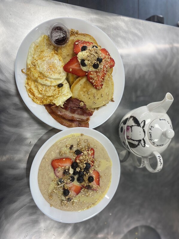 A breakfast plate with pancakes, strawberries, blueberries, and bacon, and a bowl of oatmeal with similar toppings.