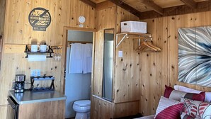 Ein holzgetäfeltes Zimmer im Blockhausstil mit einem Bett, einem Deckenventilator, einer Kaffeemaschine und einem Spiegel.