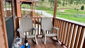 Eine Holzterrasse mit zwei Stühlen, einem Tisch, einem Stoppschild und Blick auf eine grüne Landschaft.