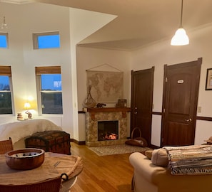 A cozy living room with a fireplace, wooden furniture, and a view of the outdoors through large windows. - On the Lake & Wine Trail & a Perfect Getaway for 16+ With an ADA Suite! (Murphysboro)