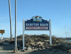 En välkomstskylt för Hampton Beach, med en strand och sanddyner i bakgrunden.