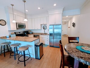 A modern kitchen with white cabinets, stainless steel appliances, a granite countertop, and bar stools.