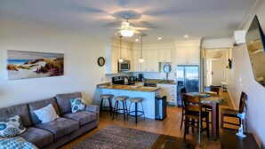 Eine moderne Küche mit weißen Schränken, einer zentralen Kochinsel mit Barhocker und einem Essbereich mit Holztisch und Stühlen.