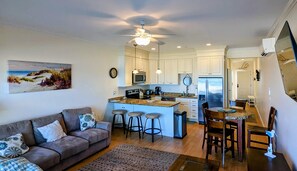 A modern kitchen with white cabinets, a central island with bar stools, and a dining area with a wooden table and chairs.