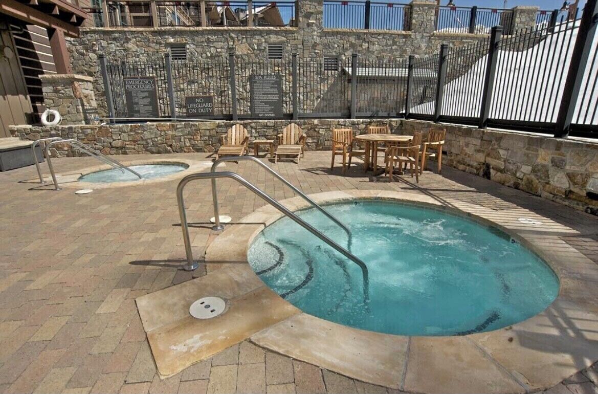 Un área de piscina con dos jacuzzis, muros de piedra y mobiliario exterior.