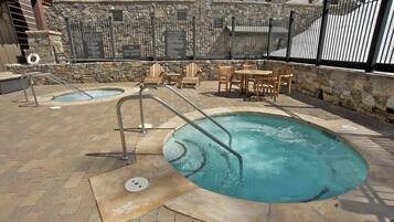 Un área de piscina con dos jacuzzis, muros de piedra y mobiliario exterior.