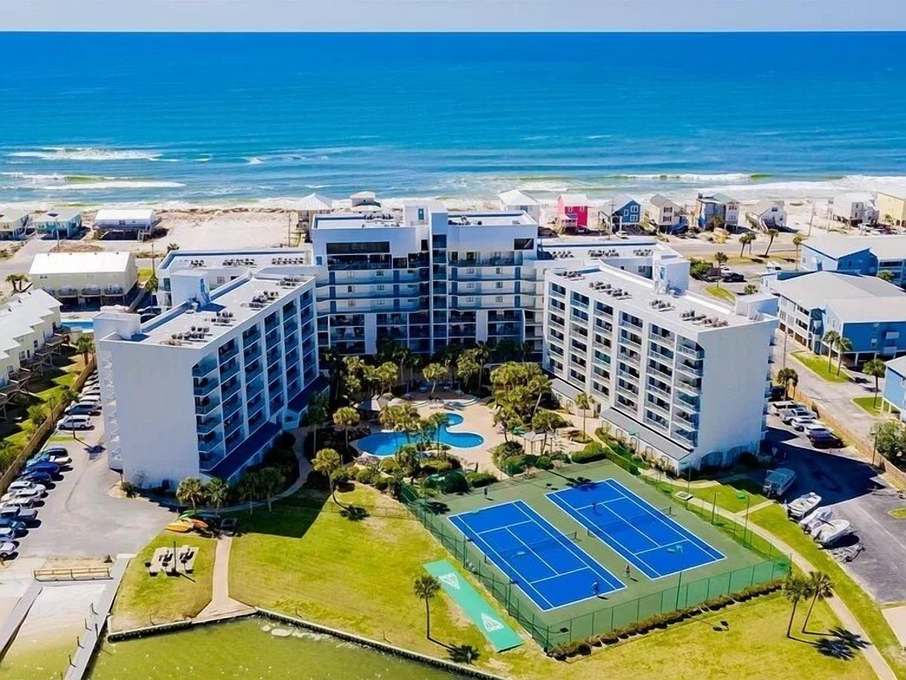 Un hotel de varios pisos con piscina, canchas de tenis y vistas al océano.