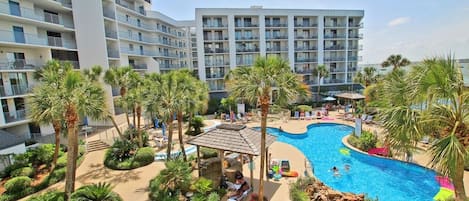 Un hotel con una piscina grande, palmeras y una zona de estar techada.