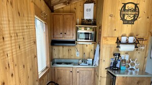 A compact kitchenette with wooden cabinets, a microwave, a coffee maker, and a small dining table with chairs. - Tiny Cottages in Cloudcroft / Mayhill NM (Mayhill)