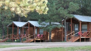 A row of wooden cabins with metal roofs, each featuring a porch and stairs leading to the entrance. - Tiny Cottages in Cloudcroft / Mayhill NM (Mayhill)