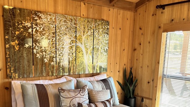 A wooden-paneled bedroom with a large bed, multiple pillows, a wall-mounted artwork, and a window with blinds. - Tiny Cottages in Cloudcroft / Mayhill NM (Mayhill)