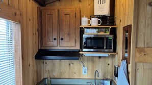 A compact kitchen with wooden cabinets, a microwave, a stove, and a sink. - Tiny Cottages in Cloudcroft / Mayhill NM (Mayhill)