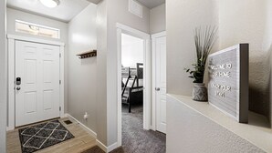 A hallway with a white door, a small shelf, a welcome sign, and a plant. - ❃Close to the POOL! 3BD/2BA! Close to BSU/Nampa/Kuna! Your Boise Vacation Spot!❃ (Meridian)