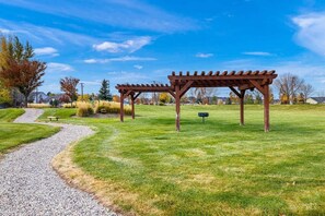 Un'area verde curata con un vialetto in ghiaia che conduce a una struttura in legno, una pergola.